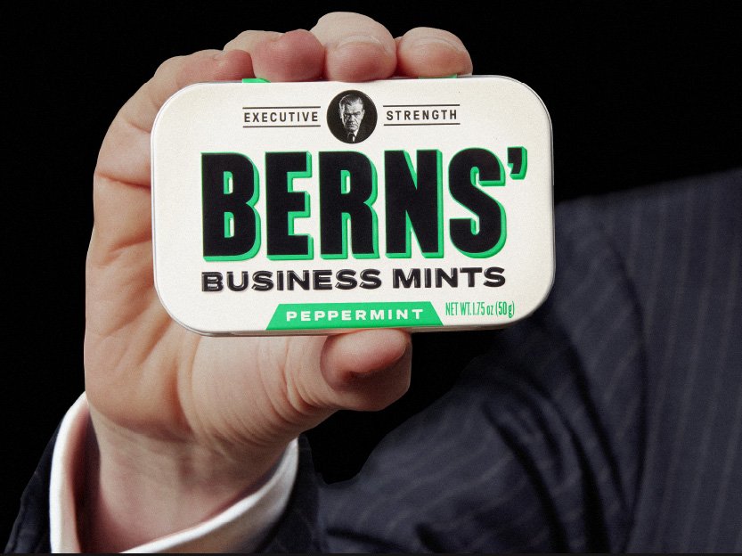 Hand holding a tin of Berns' Business Mints against a black background.